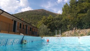 A swimming pool with a mountain in the background, a building with balconies, and trees around. - 'Carrubo' Apartment with Sea View, Wi-Fi and Air Conditioning (Ceriale)