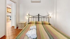 A bedroom with a bed, a bedside table, a wall-mounted air conditioner, and a view into the kitchen. - 'Carrubo' Apartment with Sea View, Wi-Fi and Air Conditioning (Ceriale)