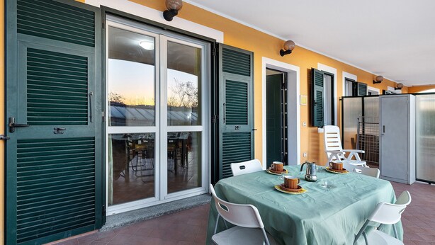 A dining area with a table set for two, a refrigerator, and a sliding glass door with shutters. - Apartment 'Ginestra' with Mountain View, Wi-Fi and Air Conditioning (Ceriale)