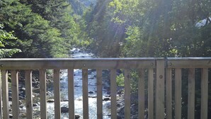 A wooden deck overlooking a river with surrounding dense forest and mountains in the background. - Mountain chalet with central fireplace 10 min from Saint-Lary and 30 from Piau (Aragnouet)