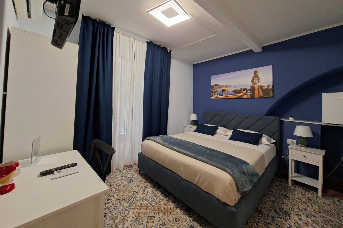 A bedroom with a bed, bedside tables, a desk, and a TV.