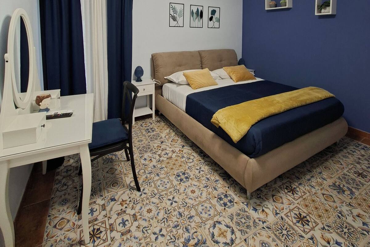 A bedroom with a bed, a desk, a chair, a mirror, and a wall-mounted air conditioner.