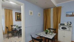 A dining area with a table and chairs, a kitchen area with a microwave and kettle, and a patterned floor. - B&B Piazza Mazzini (Catania)