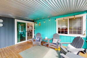 A covered patio with Adirondack chairs, a small table, and a window with blinds.