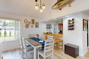 A dining area with a wooden table, white chairs, a chandelier, and a fish decoration on the wall. - Quiet 3BR Retreat, EV Charger, Fenced Yard (Tide) (Westport)