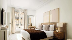 Une chambre d’hôtel avec un grand lit, une table de chevet avec une lampe, une commode et un téléviseur fixé au mur.