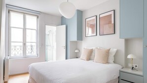 Un dormitorio con una cama grande, mesitas de noche, un armario y una ventana con balcón.