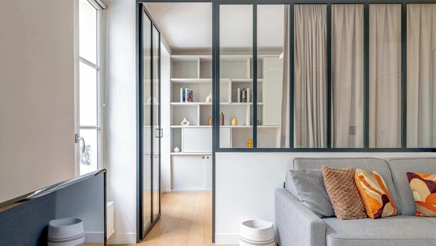 Una sala moderna con un sofá gris, una partición de vidrio y una estantería empotrada.