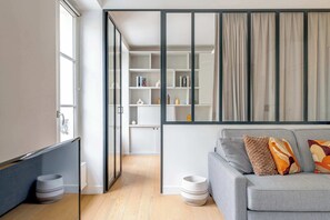 Ein modernes Wohnzimmer mit einem grauen Sofa, einer Glastrennwand und einer integrierten Bücherreoliste.