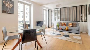 Una sala de estar moderna con una mesa de comedor de cristal, sofá gris y un ventanal grande.