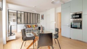 Una cocina moderna con electrodomésticos integrados, una mesa de comedor de vidrio y una zona de estar acogedora con sofá y sillones.