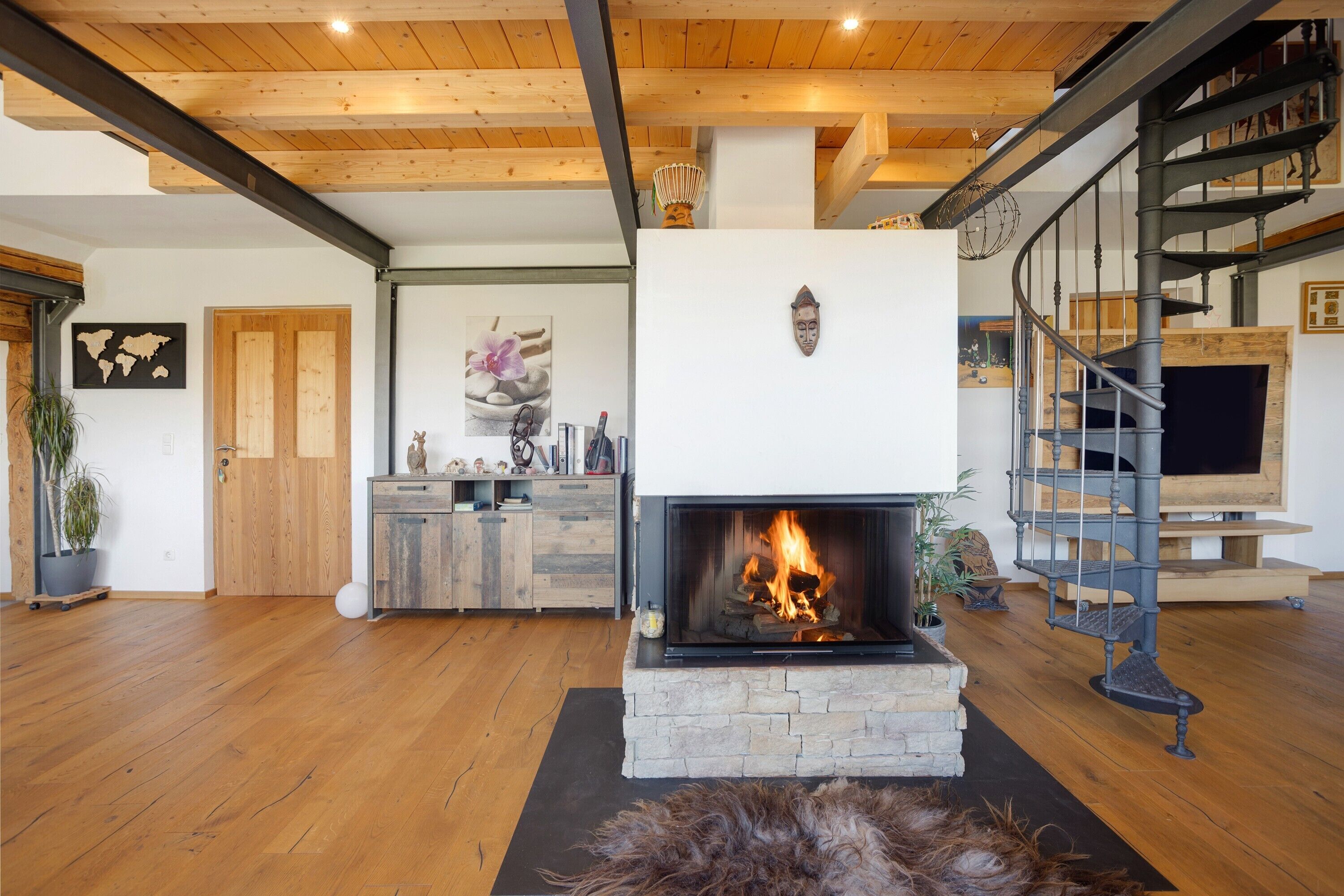 A modern living room with a fireplace, wooden floors, a staircase, and a view of the outdoors.