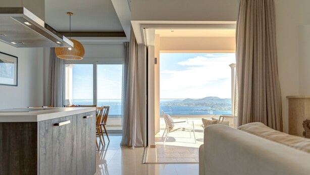 Une chambre d’hôtel moderne dotée d’un coin cuisine, d’un balcon avec vue sur la mer et d’une grande fenêtre.