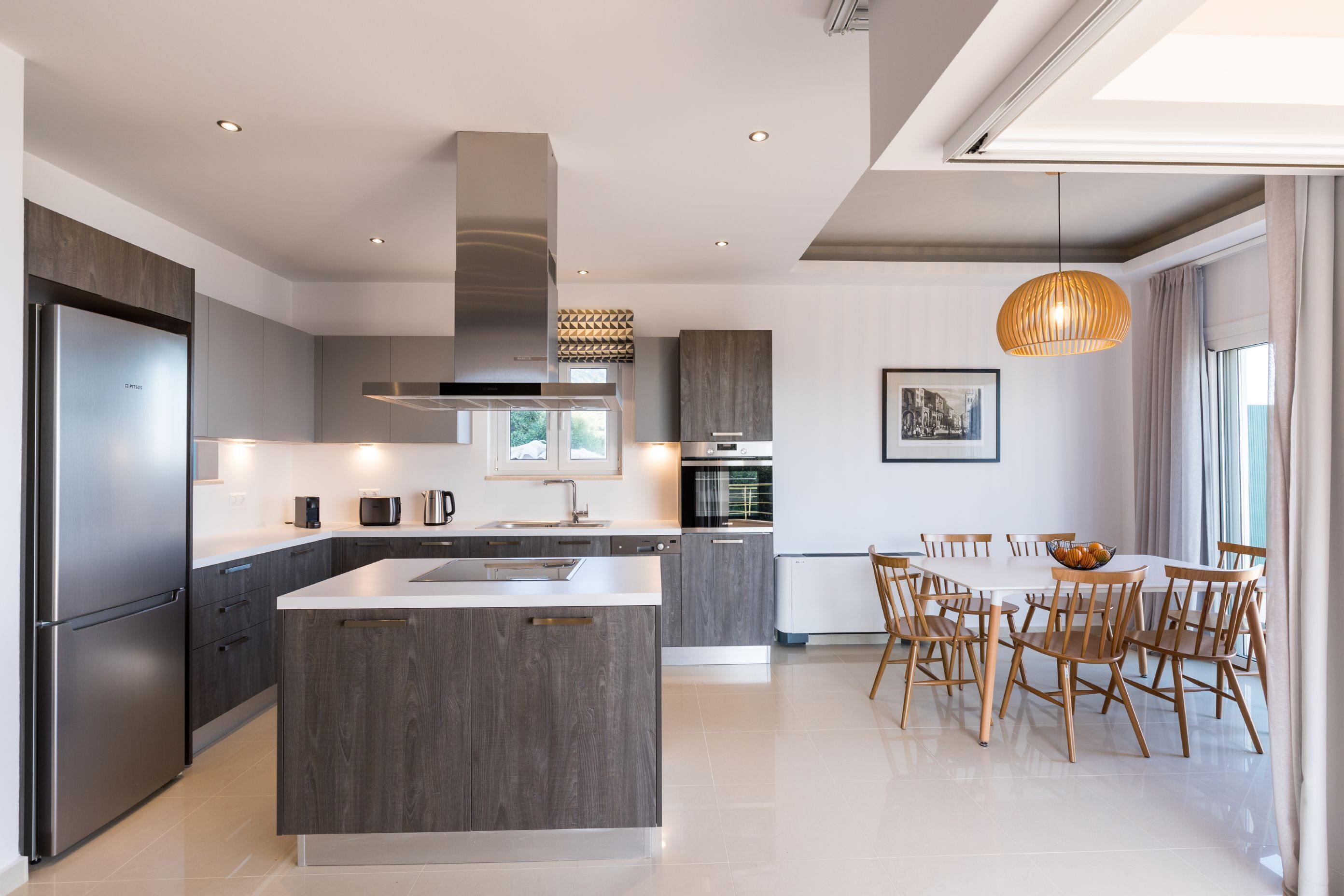 Una cocina moderna con una isla central, electrodomésticos integrados y un comedor con sillas de madera.