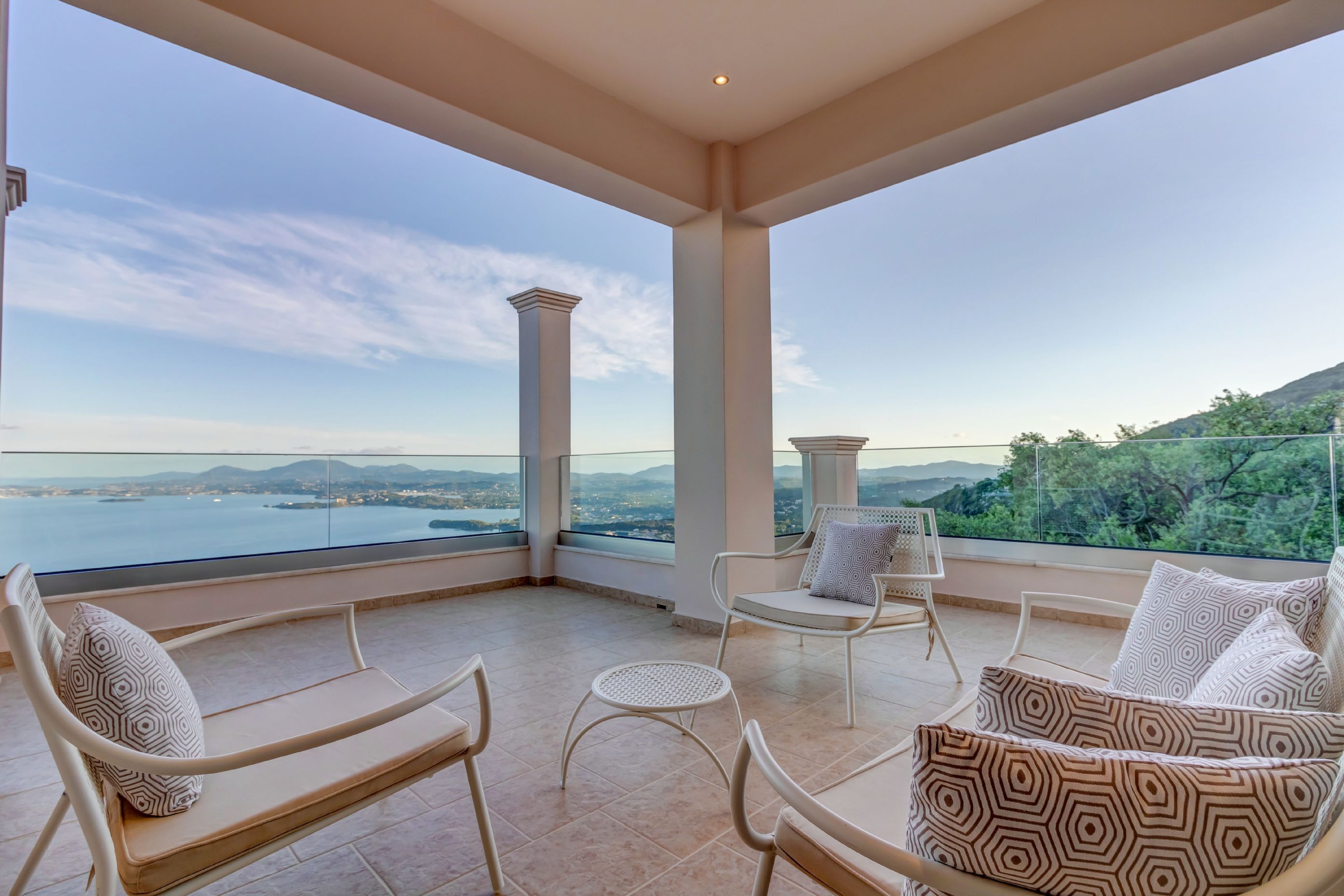 Ein Balkon mit Blick auf ein Gewässer und Hügel, möbliert mit Stühlen und einer Couch.