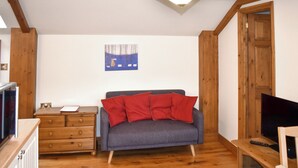 Ein gemütliches Wohnzimmer mit grauem Sofa, Holzboden, einem Gemälde an der Wand und einem Fernseher auf einem Holzschrank.