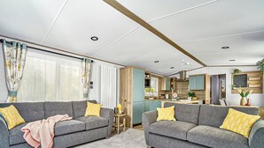 Ein modernes Wohnzimmer mit zwei grauen Sofas, einem kleinen Holztisch und einer Küchenzeile im Hintergrund.