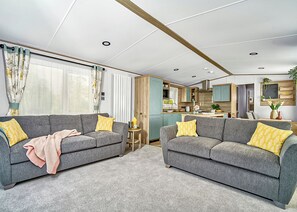 Ein modernes Wohnzimmer mit zwei grauen Sofas, einem kleinen Holztisch und einer Küchenzeile im Hintergrund.