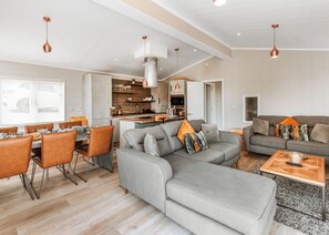 A modern living room with a grey sofa, dining table, and chairs, a kitchen area, and pendant lighting. - 3 bedroom accommodation in Bridgnorth (Bridgnorth)