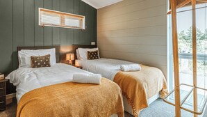 Een hotelkamer met twee bedden, een raam met zonwering, een lamp en uitzicht op het landschap.