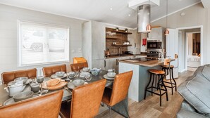 Een moderne keuken met een centraal eiland, een eetgedeelte met bruine lederen stoelen en een grijze bank.