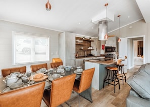Een moderne keuken met een centraal eiland, een eetgedeelte met bruine lederen stoelen en een grijze bank.