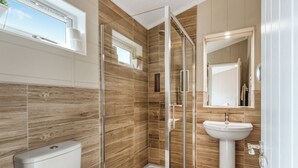 Een moderne badkamer met een douchecabine van glas, een wit toilet en een wastafel met spiegel.
