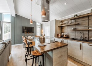 Een moderne keuken met een houten kookeiland, barstoelen, een ingebouwde wijnkast en een flatscreen-televisie.