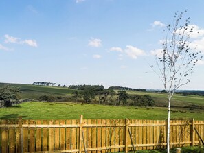Ein Holzzaun mit einem Baum im Vordergrund und einem grünen Feld im Hintergrund.