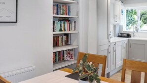 Une cuisine moderne avec des meubles blancs, une table à manger avec des chaises et une bibliothèque remplie de livres.