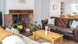 Un salon chaleureux avec une cheminée en briques, un canapé en cuir marron, une table basse en bois et une bibliothèque en arrière-plan.