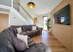 A modern living room with a sectional sofa, a large TV, a staircase, and a potted plant. - Brand new for 2026. A bespoke-built luxury lodge created for family escapes. (Fitling, Nr Hornsea)