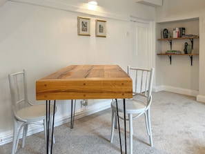 Un comedor con una mesa de madera, sillas blancas y una estantería con libros y adornos.
