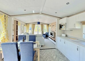 Ein kompakter, moderner Wohnraum für ein Wohnmobil mit Essbereich, Sitzgelegenheiten, einer Küchenzeile und Blick ins Freie.