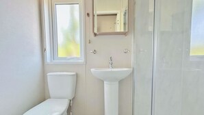 Kylpyhuone, jossa on wc, pesuallas ja lasinen suihkuseinä.