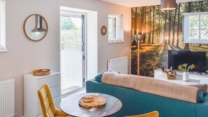A modern living room with a sofa, a round table, a television, and a forest-themed wall mural. - 1 bedroom accommodation in Lydney, Forest of dean (Lydney, Forest of dean)