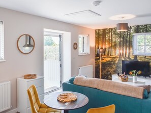 A modern living room with a sofa, a round table, a television, and a forest-themed wall mural. - 1 bedroom accommodation in Lydney, Forest of dean (Lydney, Forest of dean)