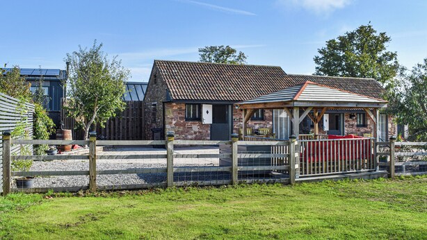 A rustic stone building with a tiled roof, a wooden fence, and a gravel pathway leading to a covered seating area. - 1 bedroom accommodation in Lydney, Forest of dean (Lydney, Forest of dean)