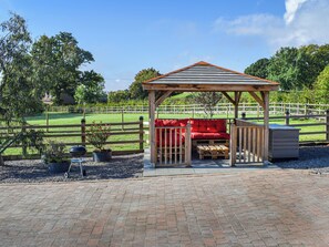 A gazebo with a red cushioned bench, surrounded by a wooden fence and gravel path. - 1 bedroom accommodation in Lydney, Forest of dean (Lydney, Forest of dean)