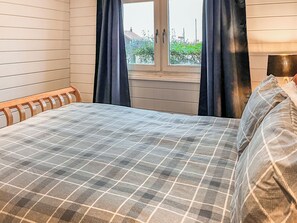 Une chambre avec un lit, une fenêtre avec des rideaux et une vue sur la verdure.