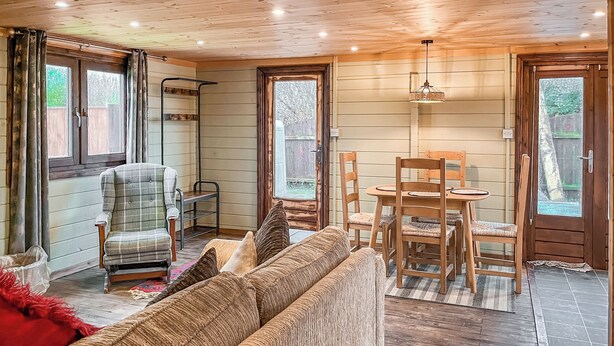 Un interior acogedor con techo de madera, un sofá, una silla, una mesa de comedor con sillas y una ventana.