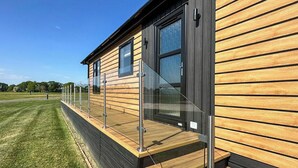 Een modern gebouw met een houten gevel, grote ramen en een glazen hekwerk op het terras.