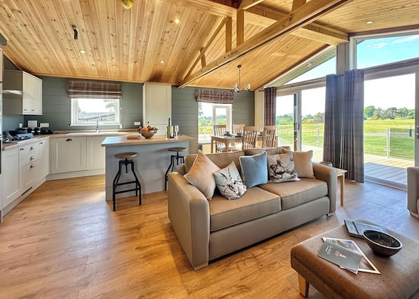 A spacious living area with a wooden ceiling, a sofa with cushions, a dining table, and a kitchen area with a bar.