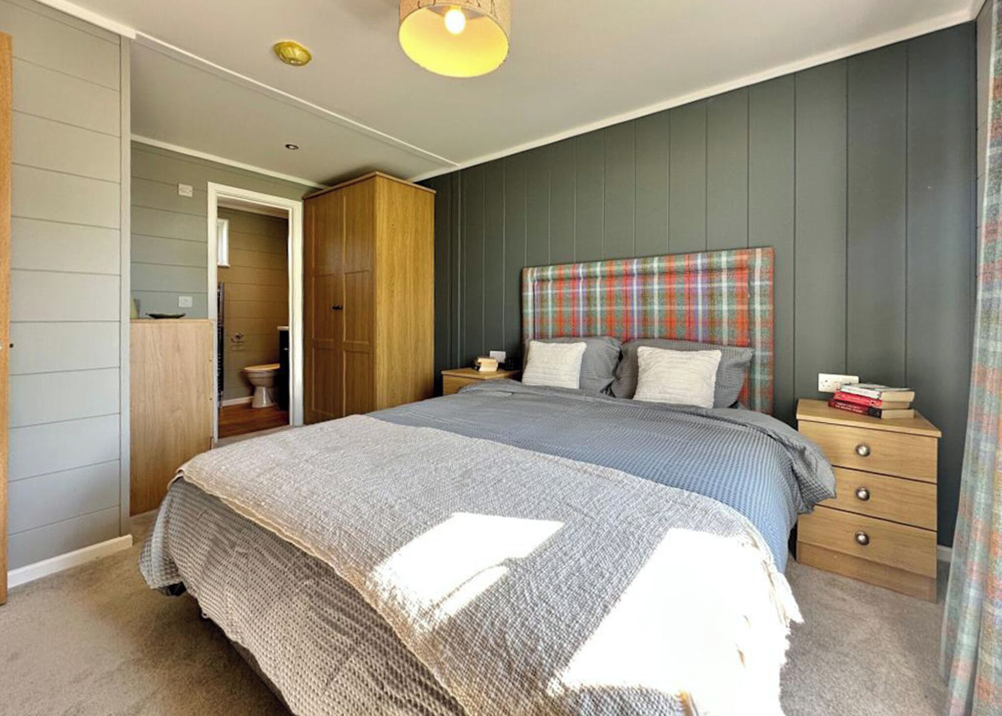Une chambre à coucher comprenant un lit, des tables de chevet, une armoire et une porte donnant accès à une salle de bain.