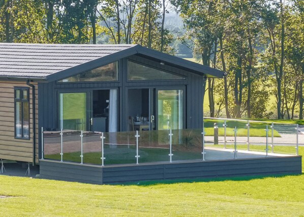 A modern house with a glass balcony, a wooden deck, and a view of trees.