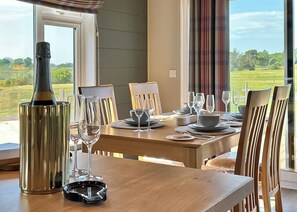 Mesa de comedor preparada para cuatro personas, con copas de vino, platos, cubiertos, una botella de vino y un candelabro.