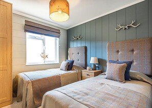 Un dormitorio con dos camas, una ventana con persianas, una lámpara en una mesita de noche y decoraciones de asta de ciervo en la pared.