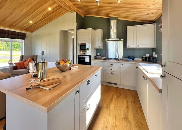 A modern kitchen with wooden cabinets, a central island, and a view of the outdoors.