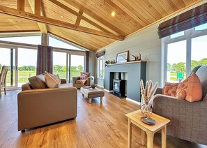 Un vaste salon doté d’une cheminée, de poutres apparentes en bois et de grandes fenêtres offrant une vue sur l’extérieur.