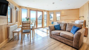 A cozy room with a sofa, a dining table, and a chair. There are large windows and a view of the outside. - 1 bedroom accommodation in Ripponden (Ripponden)